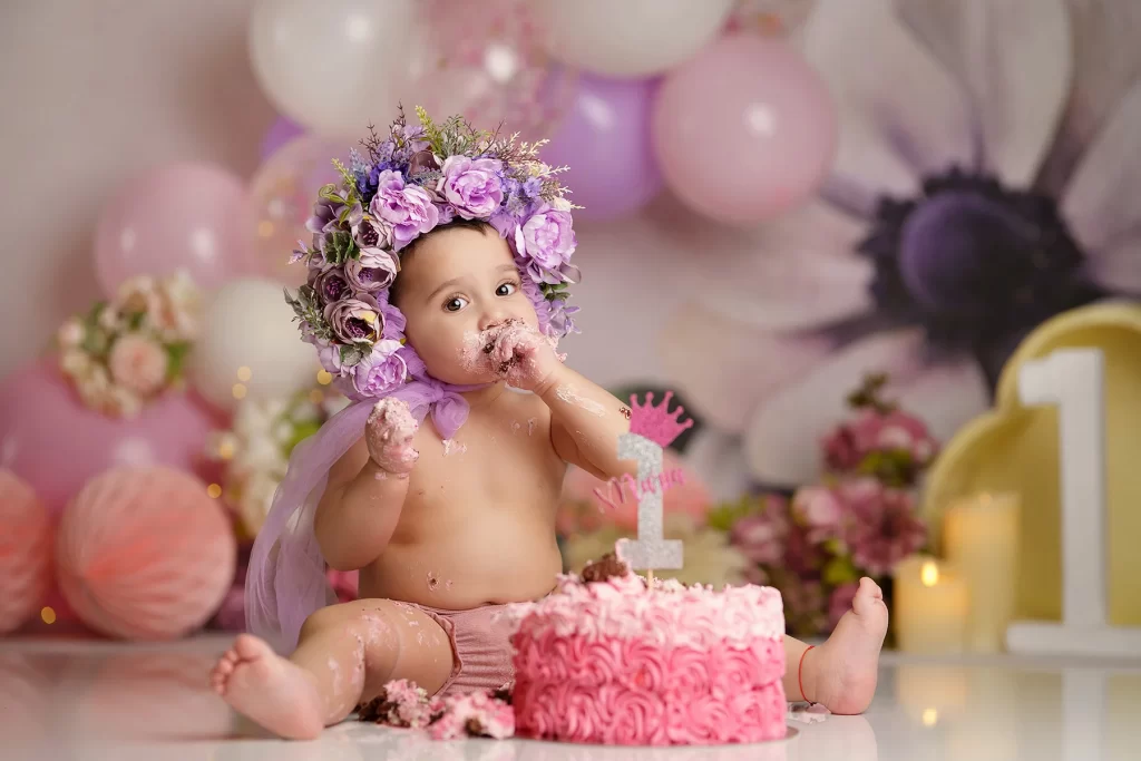 Cake Smash Photoshoot – Mihaela Mocanasu Photography Cake smash photoshoot with a baby girl wearing a flower crown, enjoying her first birthday cake in a pastel pink setting – joyful cake smash photography by Mihaela Mocanasu, Stanmore.