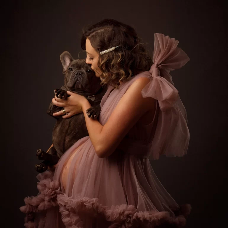 Expectant mother cuddling French Bulldog; soft curls and pearl hair clip.