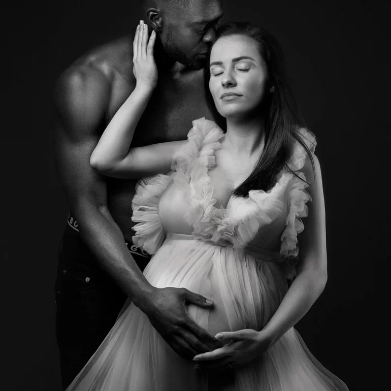 B&W couple’s embrace; ruffled gown and protective forehead kiss.