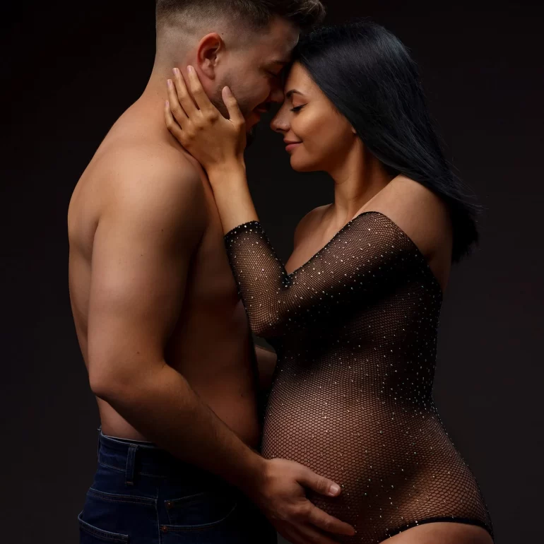Sheer black bodysuit; intimate forehead touch with partner; dark tones.