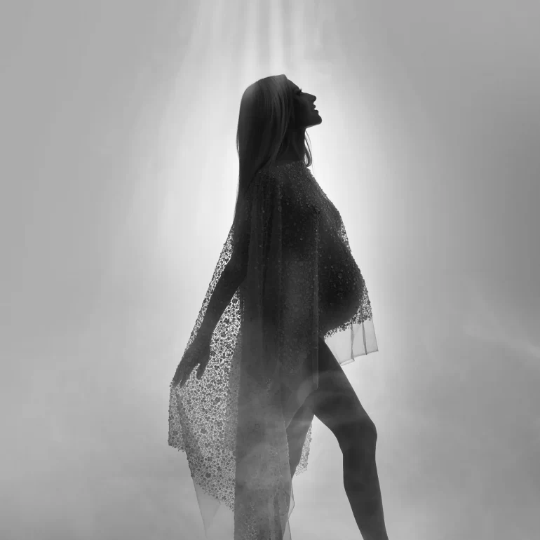 Backlit silhouette in shimmering sheer fabric; divine, misty glow.