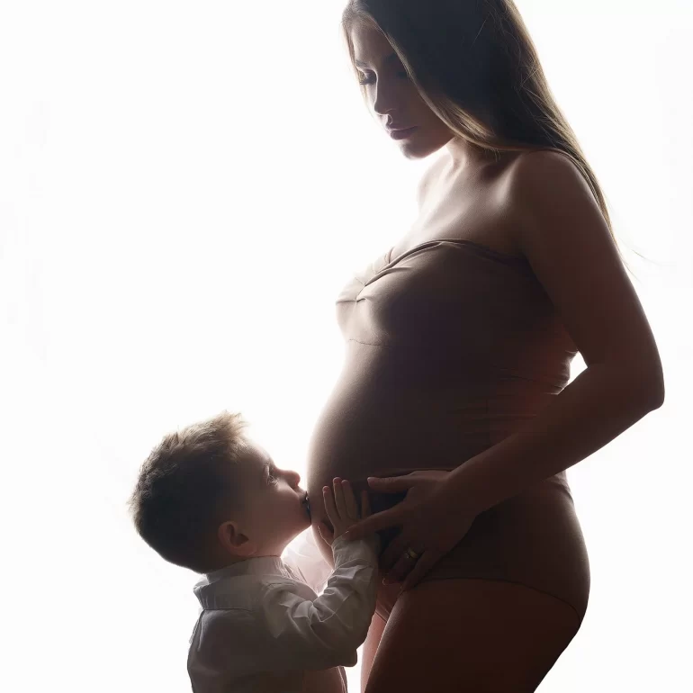 Backlit silhouette of mother and young son; kiss on the belly.