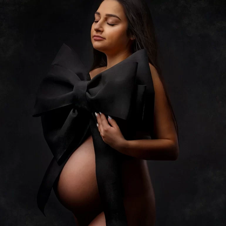 Oversized black bow; closed eyes and calm expression; textured dark background.