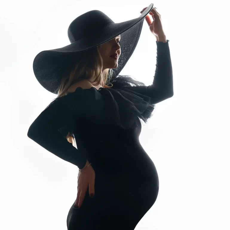 Off‑shoulder black dress and wide‑brim hat; high‑contrast silhouette.