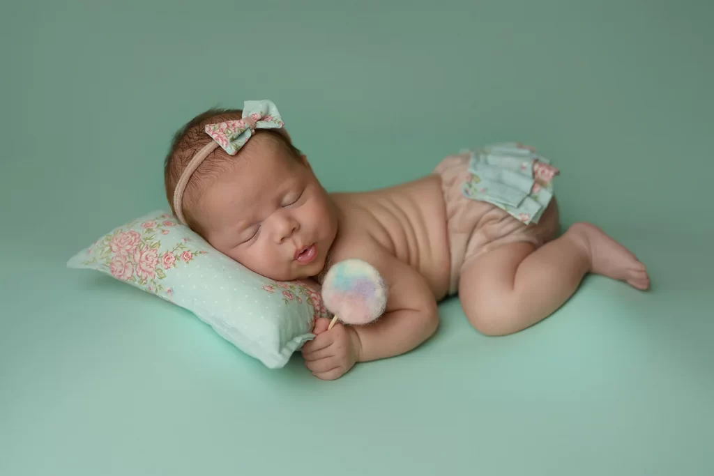 Newborn Photoshoot – Mihaela Mocanasu Photography Newborn baby girl sleeping peacefully on a mint background, holding a soft pom-pom – fine art newborn photography at Mihaela Mocanasu Photography, Stanmore.