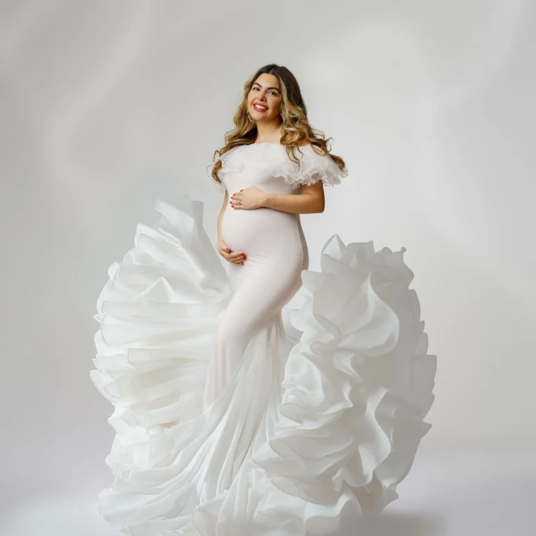 Flowing white off‑shoulder gown with dramatic ruffles; joyful smile.