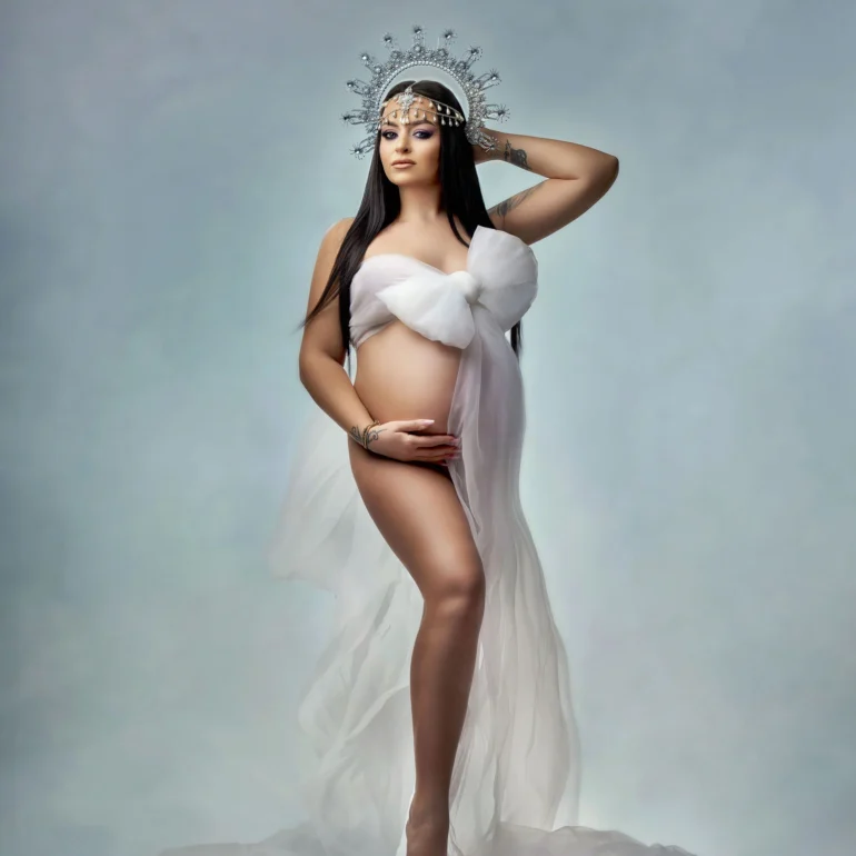 White bow‑styled fabric and crystal crown; barefoot on soft blue.
