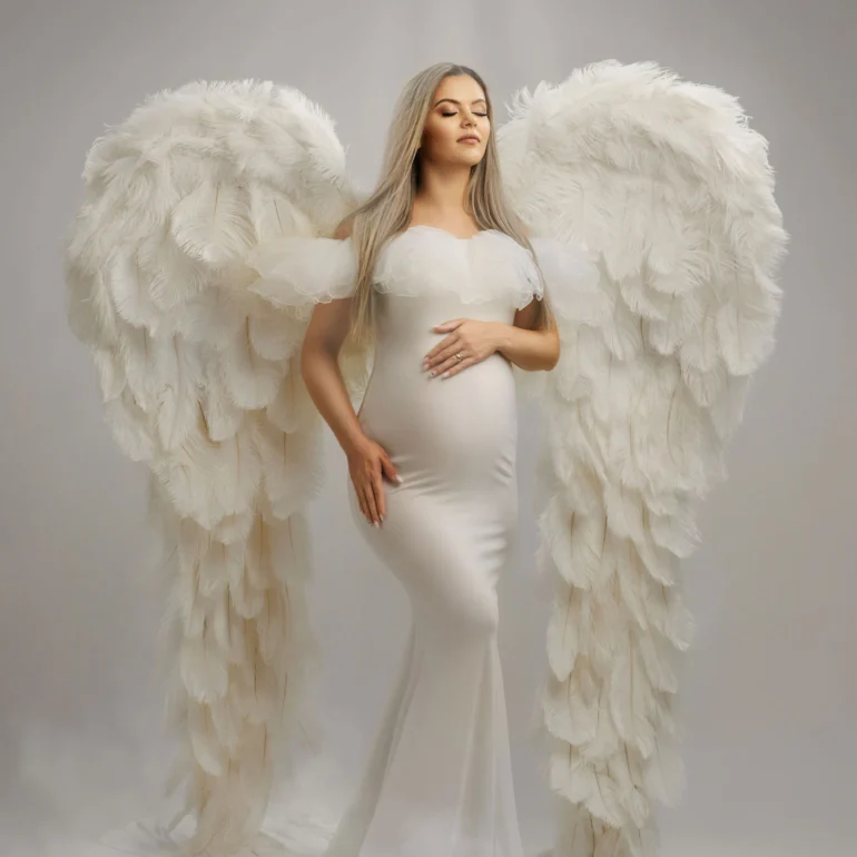 Sleek white gown and white feathered wings; glowing white backdrop.