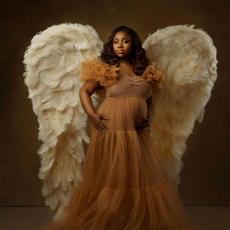 Amber‑toned layered gown and large wings; heavenly studio presence.