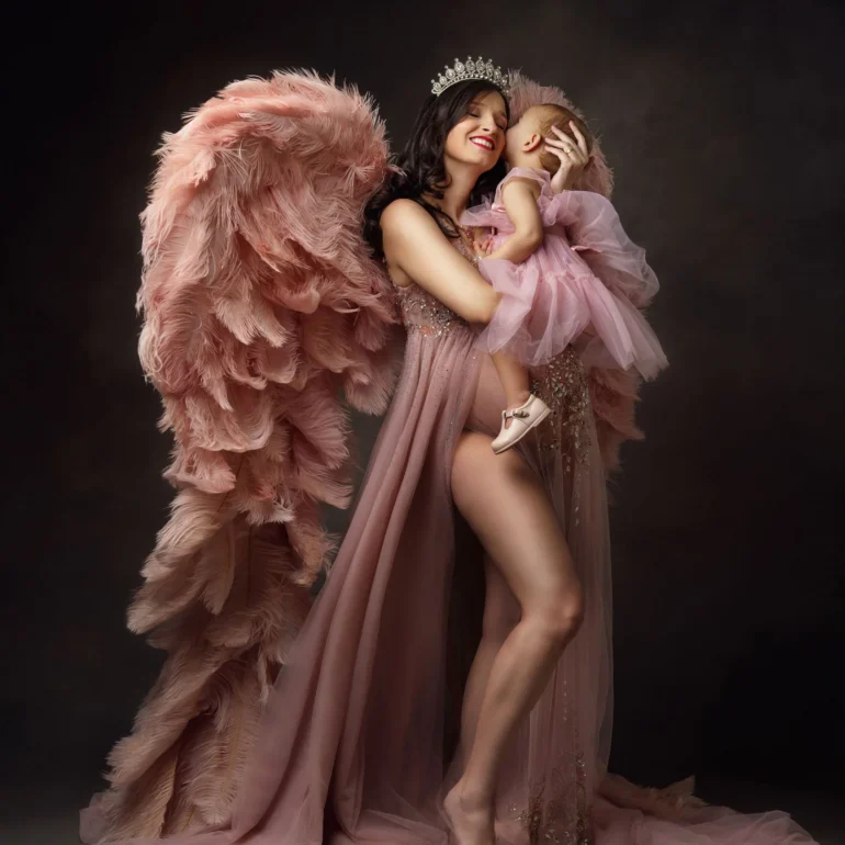 Mother with child in coordinated pink; soft feathered wings; tender moment.