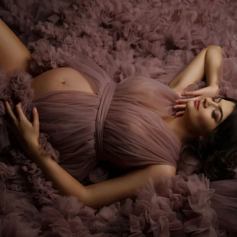Reclining on mauve ruffles; closed eyes; tranquil, intimate light.