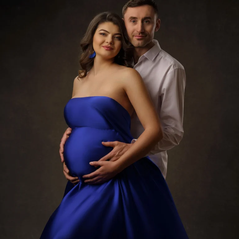 Royal‑blue strapless gown; tender embrace from behind; warm light.